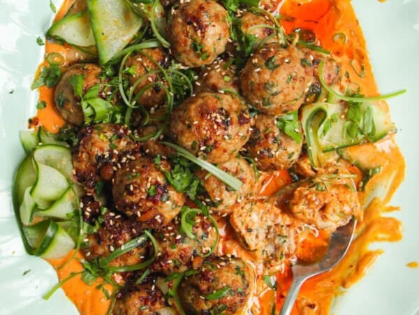 Dumpling meatballs on gochuajang sauce with pickled cucumber on an oval platter.