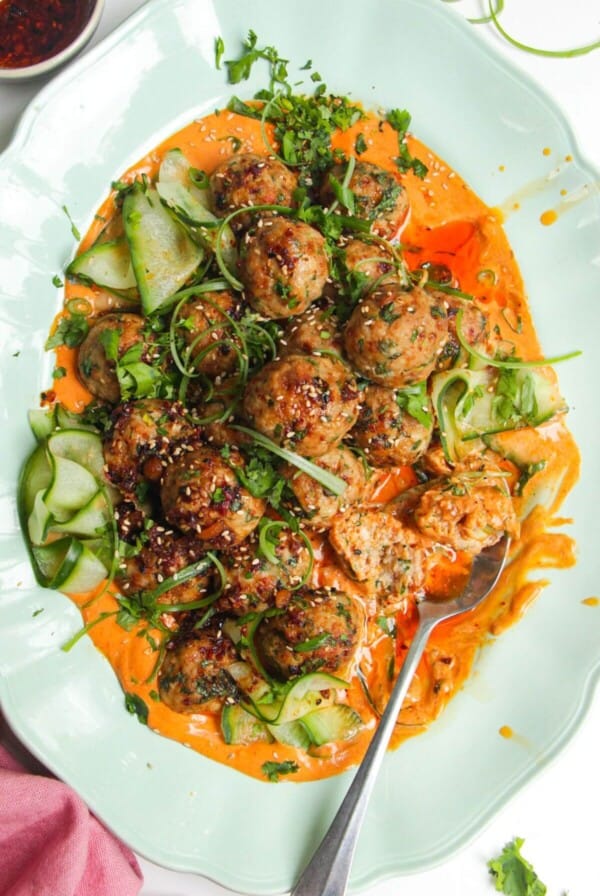 Dumpling meatballs on gochuajang sauce with pickled cucumber on an oval platter.