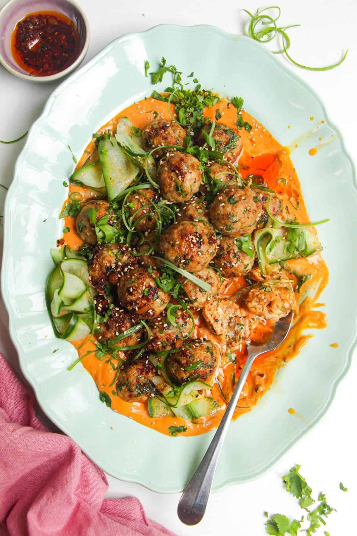 Dumpling meatballs on gochuajang sauce with pickled cucumber on an oval platter.