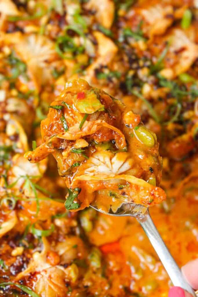 Spoon with two baked dumplings in sauce on it.