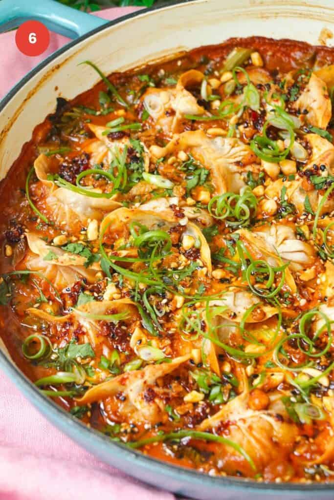 Baked dumplings in satay sauce in a skillet with chili oil on top.