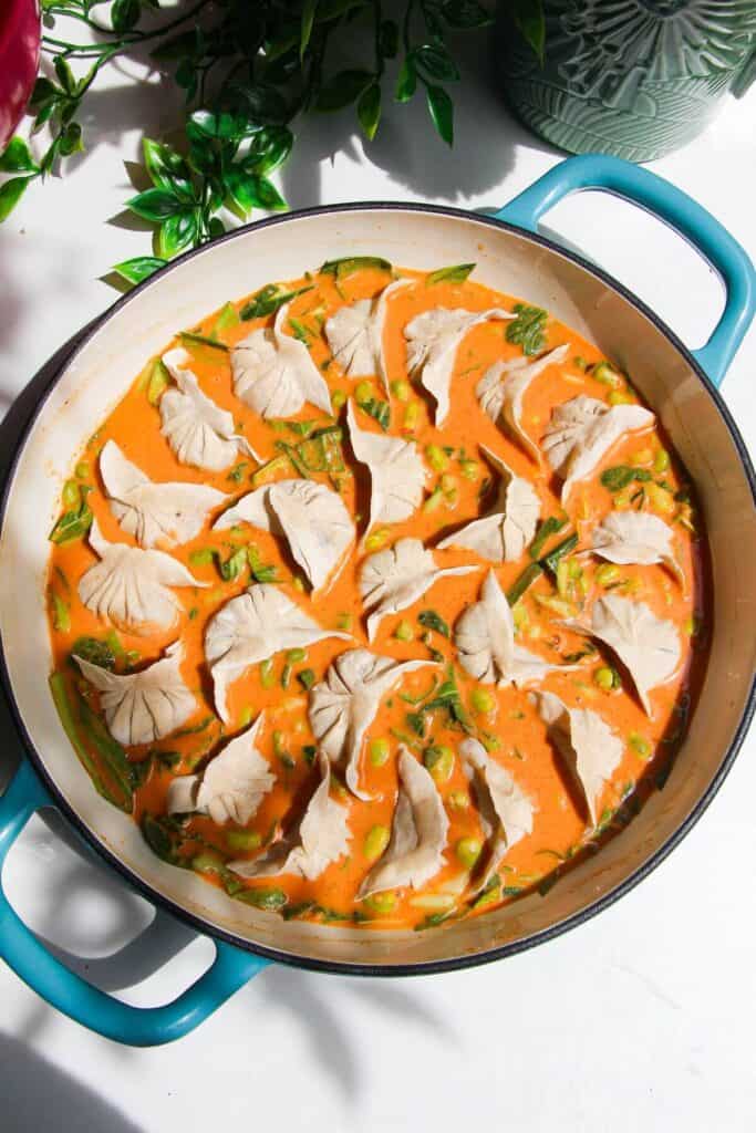 Frozen dumplings assembled in satay sauce in skillet.