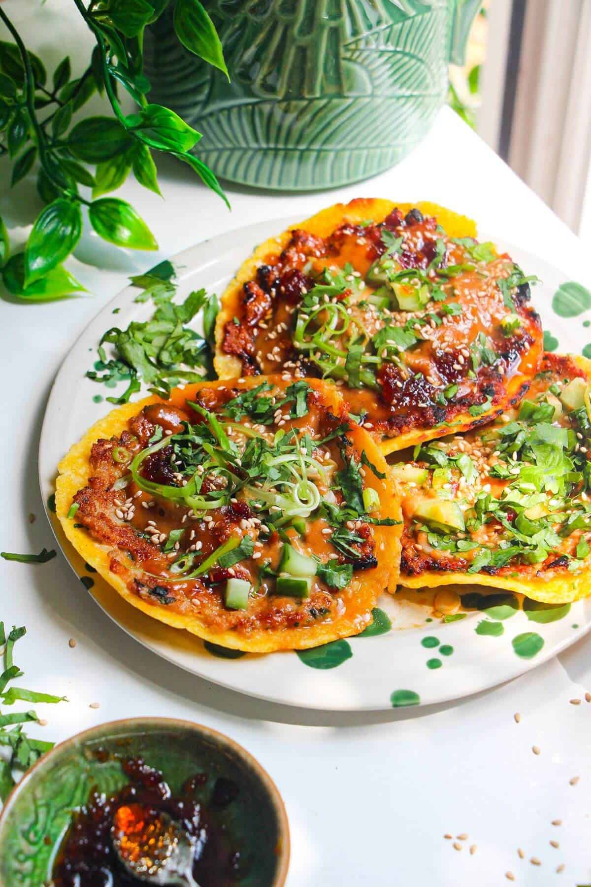 Three smash satay tacos on a white and green plate with sweet chili and satay sauce on the side.