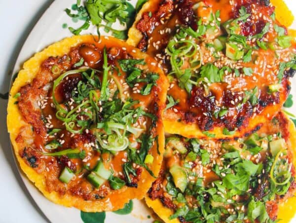 Three smash satay tacos on a white and green plate with sweet chili and satay sauce on the side.