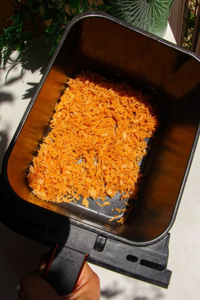 Seasoned rice in air fryer basket.