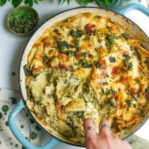 Hand serving green goddess lasagna from a large skillet.