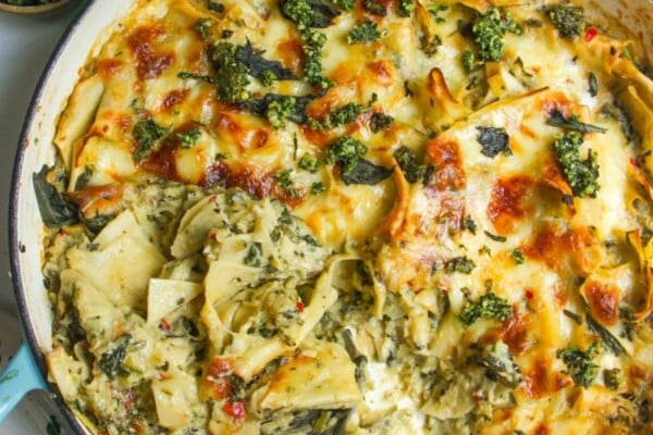 Hand serving green goddess lasagna from a large skillet.