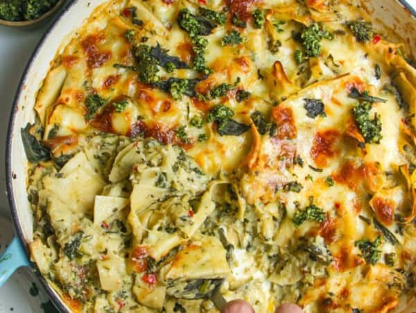 Hand serving green goddess lasagna from a large skillet.