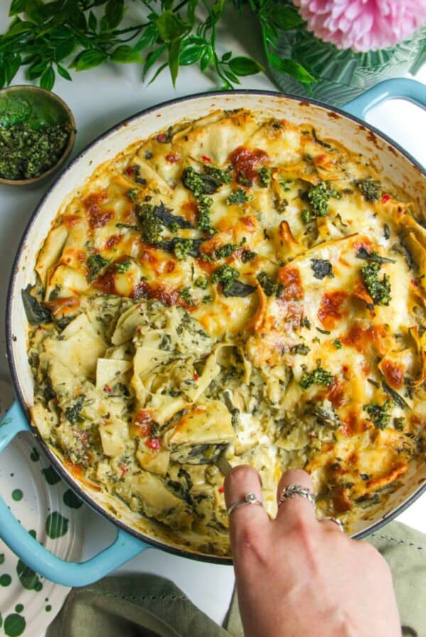 Hand serving green goddess lasagna from a large skillet.