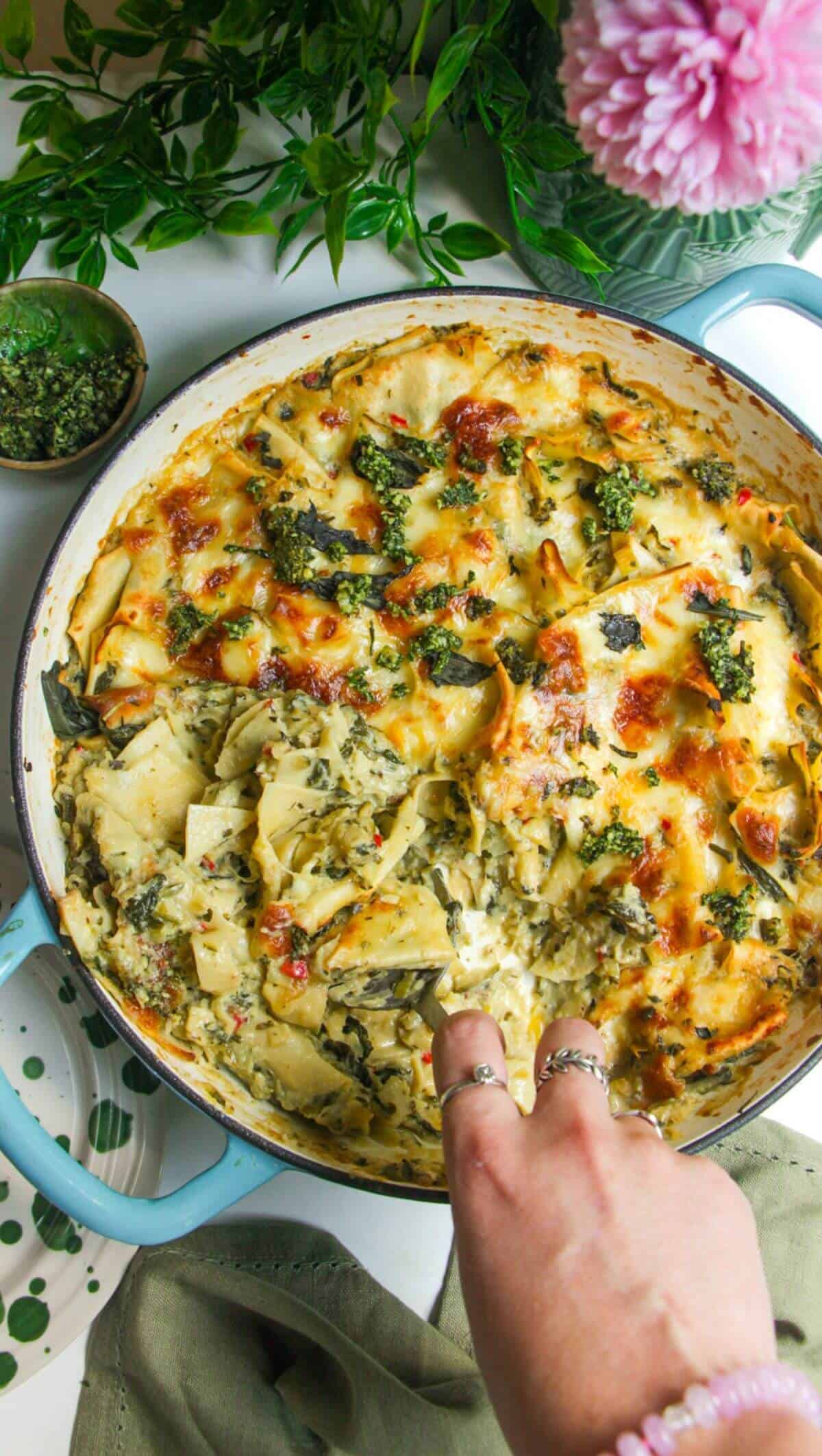 Hand serving green goddess lasagna from a large skillet.