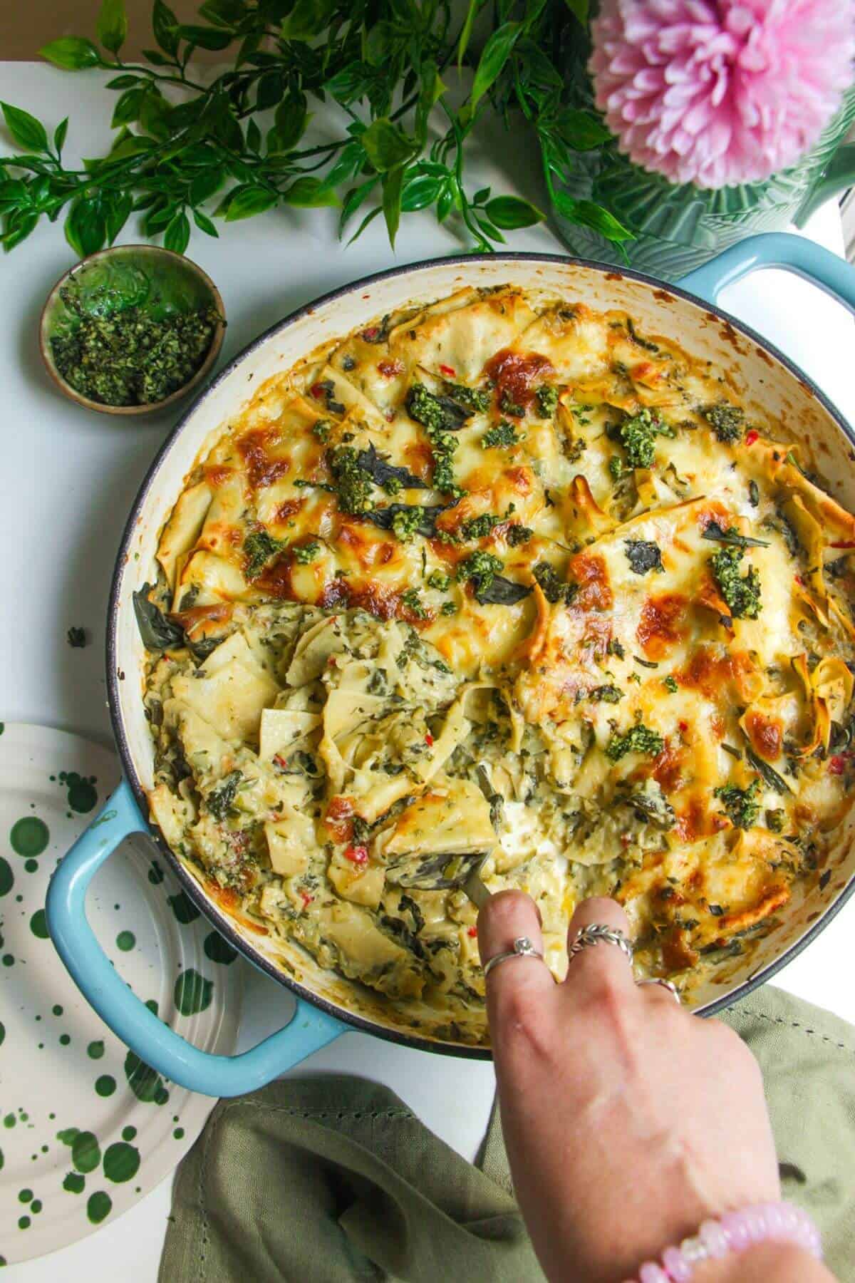 Hand serving green goddess lasagna from a large skillet.