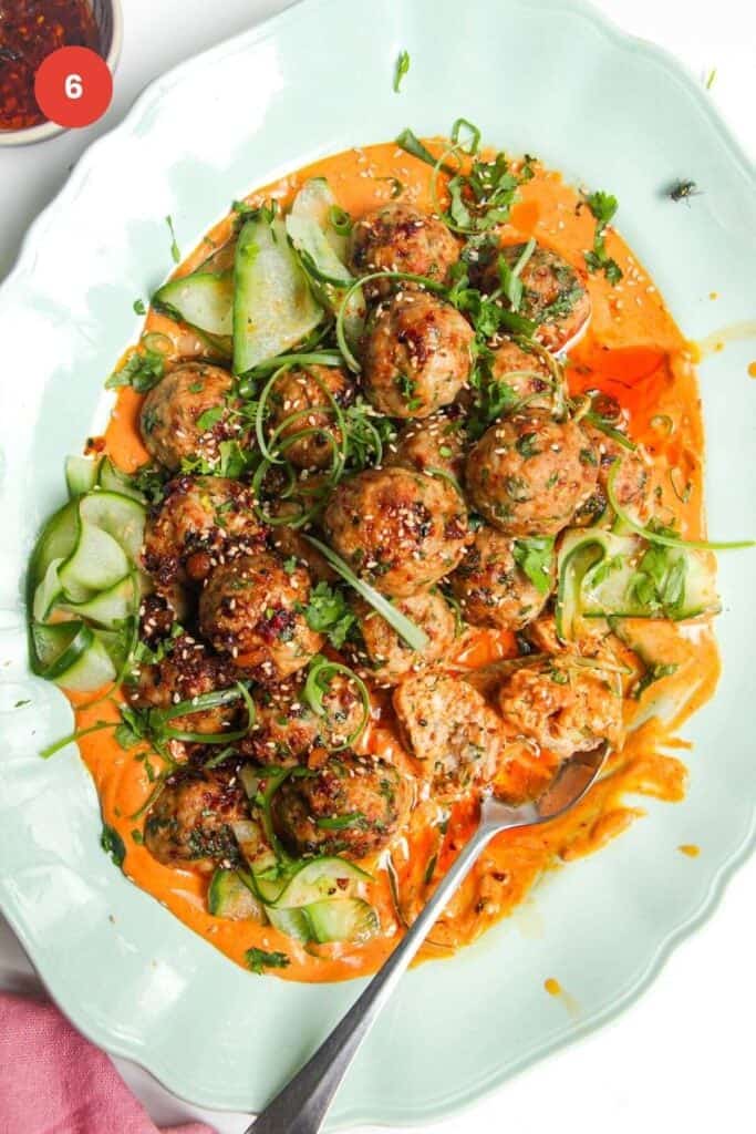 Dumpling meatballs on gochuajang sauce with pickled cucumber on an oval platter.