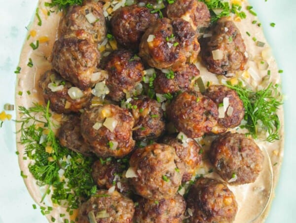 Cheeseburger meatballs on burger sauce on a platter.