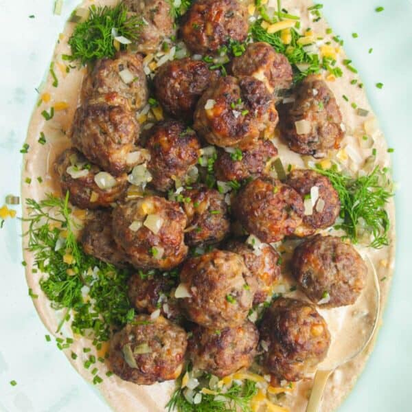 Cheeseburger meatballs on burger sauce on a platter.