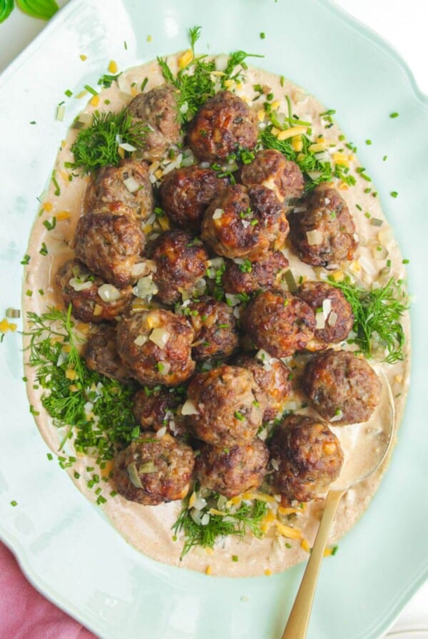 Cheeseburger meatballs on burger sauce on a platter.