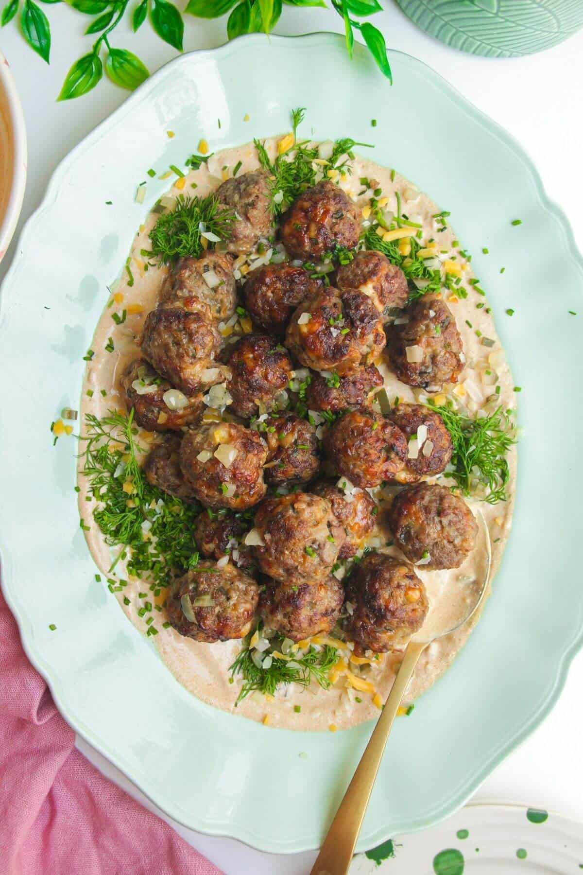 Cheeseburger meatballs on burger sauce on a platter.