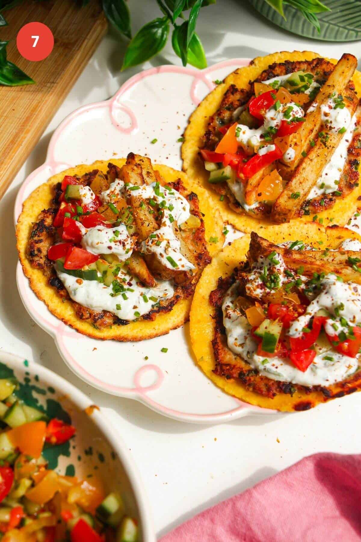 Three chicken gyros tacos topped with tzatziki, salad and fries on a plate.