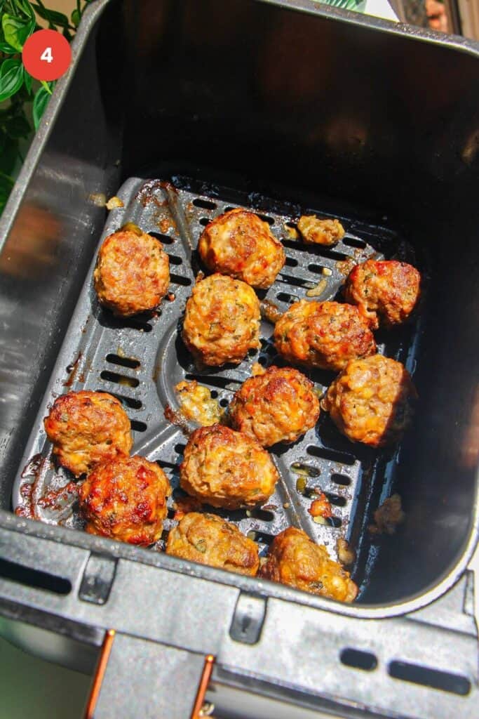 Cooked cheeseburger meatballs in air fryer basket.