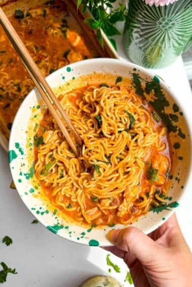 Holding bowl with baked satay ramen in it, with chopsticks.