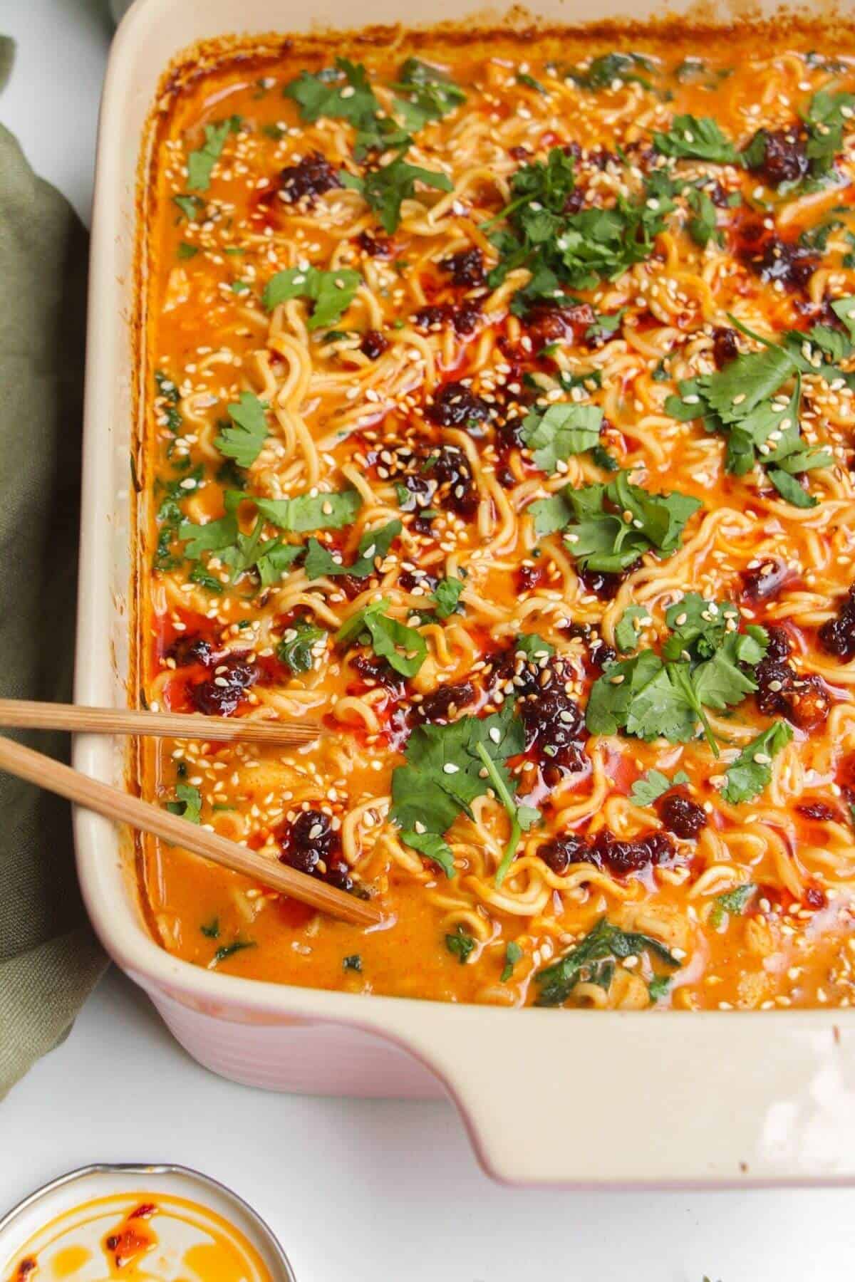 Baked satay ramen in an oven dish, with chopsticks on the side.