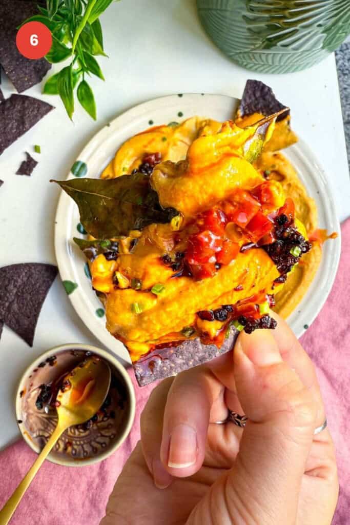 Holding tortilla chip with butternut squash feta dip on it.