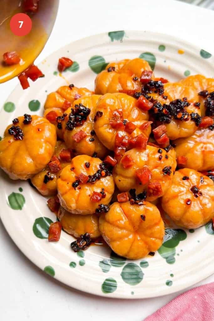 Crispy chorizo on top of pumpkin shaped gnocchi on plate.