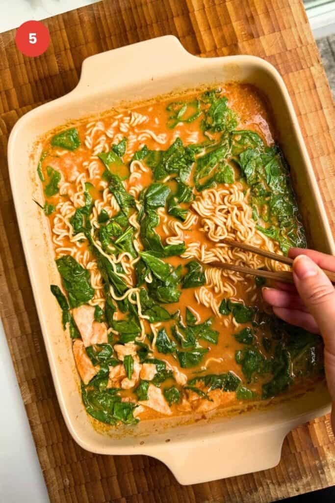 Hand holding chopsticks, mixing ramen noodles.