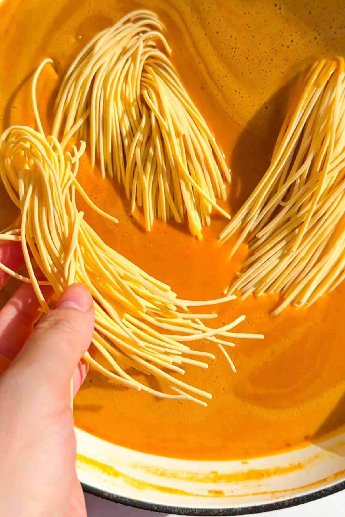 Adding noodles to butternut squash coconut broth.