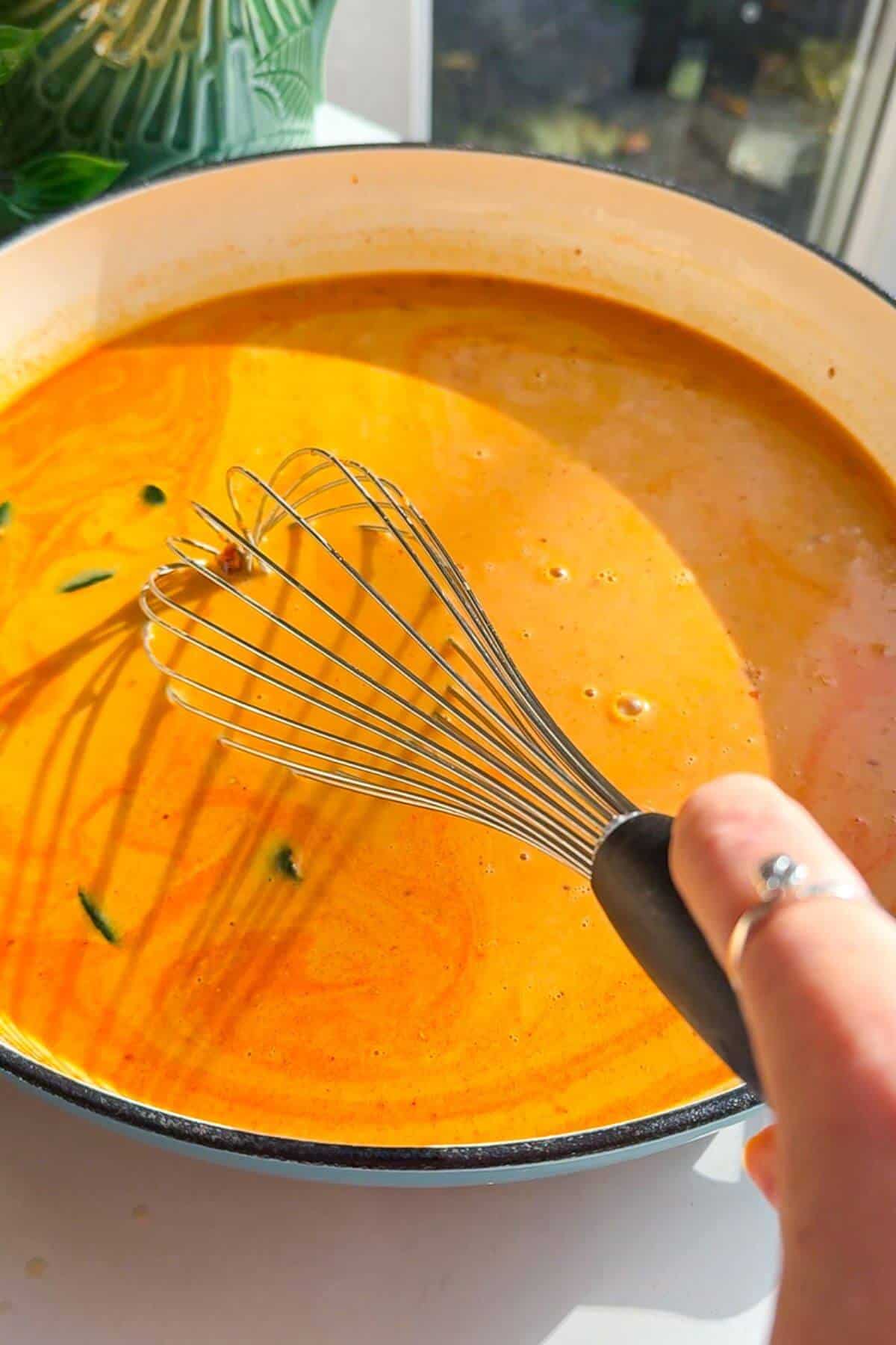 Whisking coconut gochujang broth in pan.