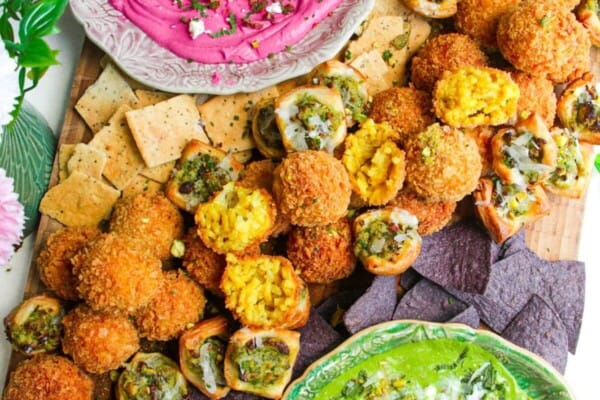 Dips, arancini and puff pastry bites on a wooden board.