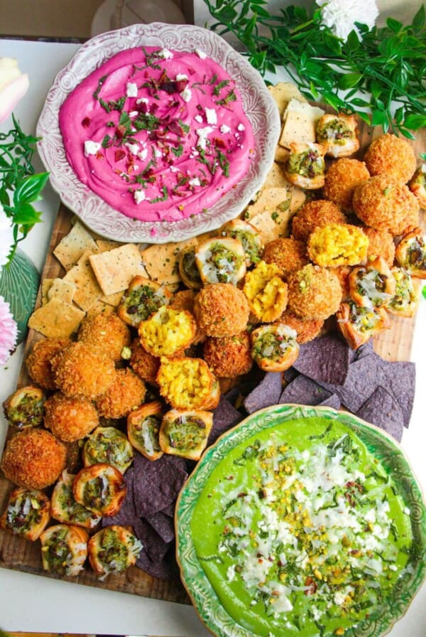 Dips, arancini and puff pastry bites on a wooden board.