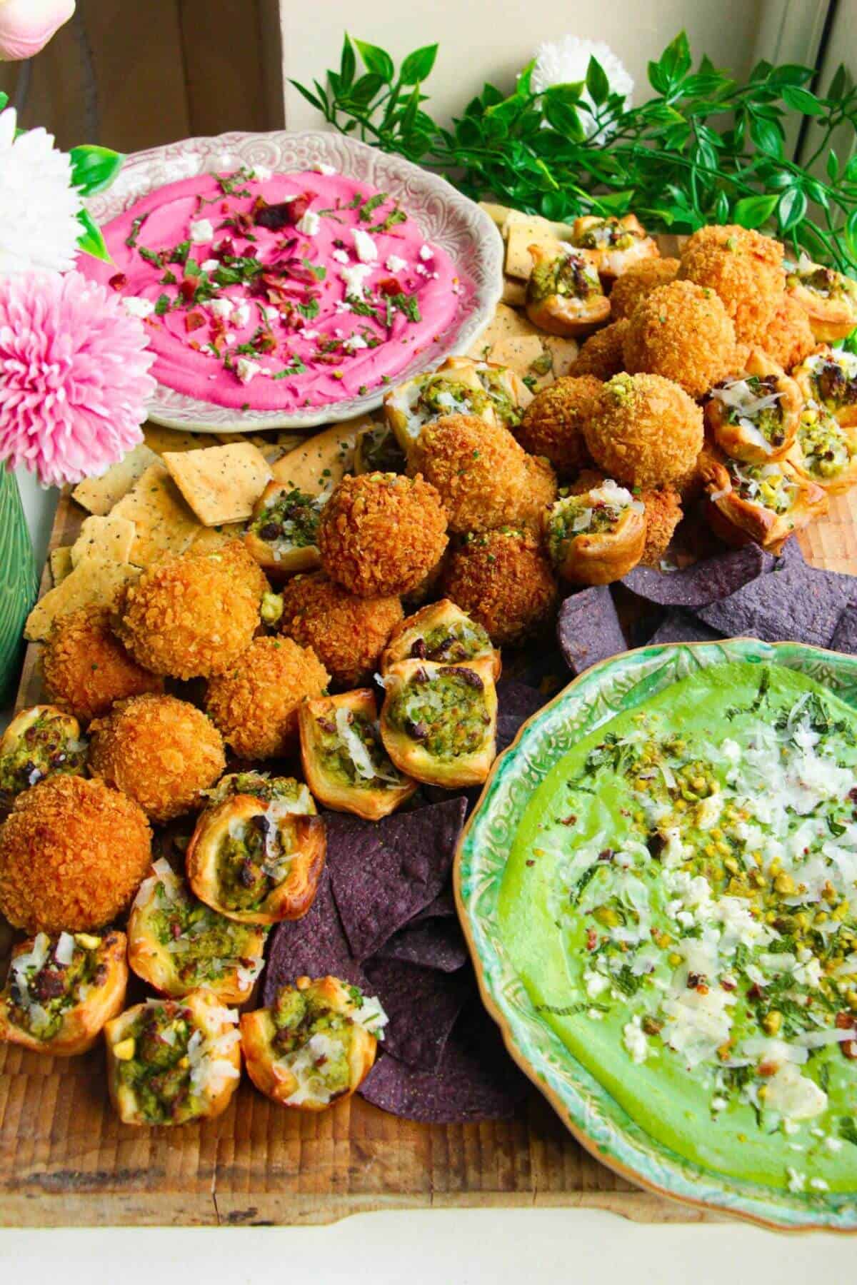 Dips, arancini and puff pastry bites on a wooden board.