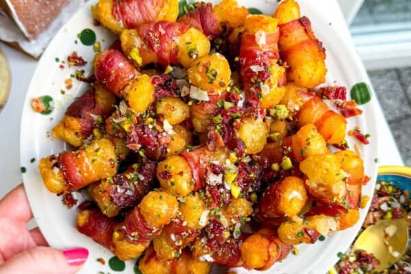 Bacon wrapped tater tots drizzled with honey and nuts on a plate.