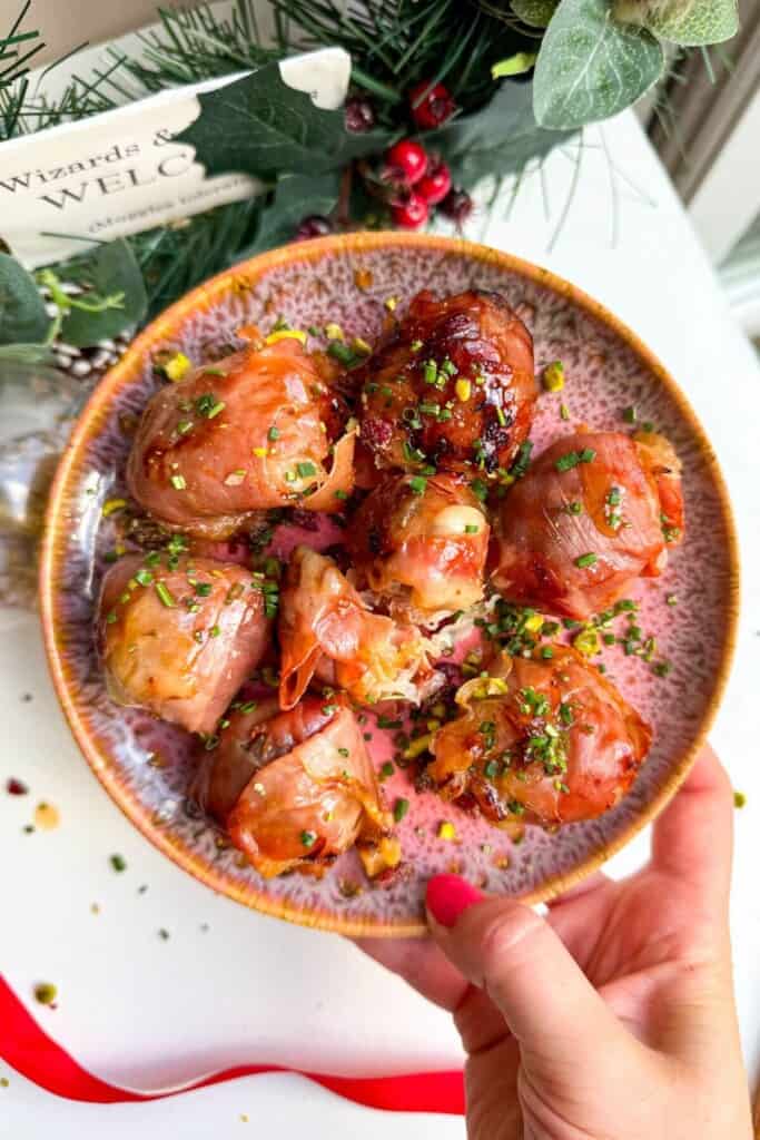 Hand holding plate of brie, prosciutto bombs.