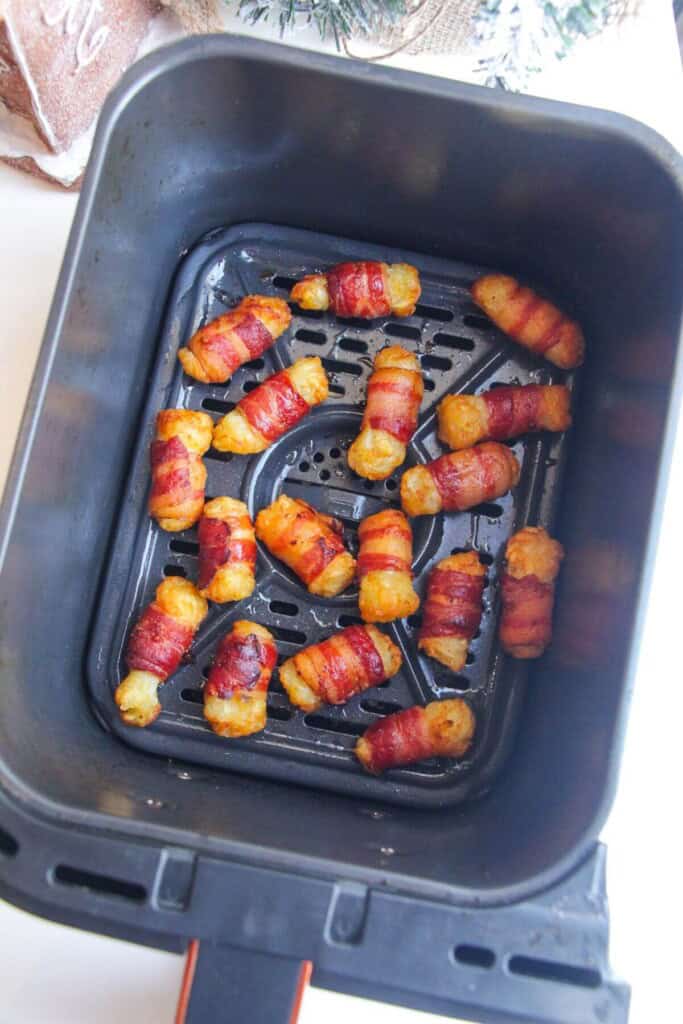 Crispy bacon wrapped tater tots in air fryer basket.