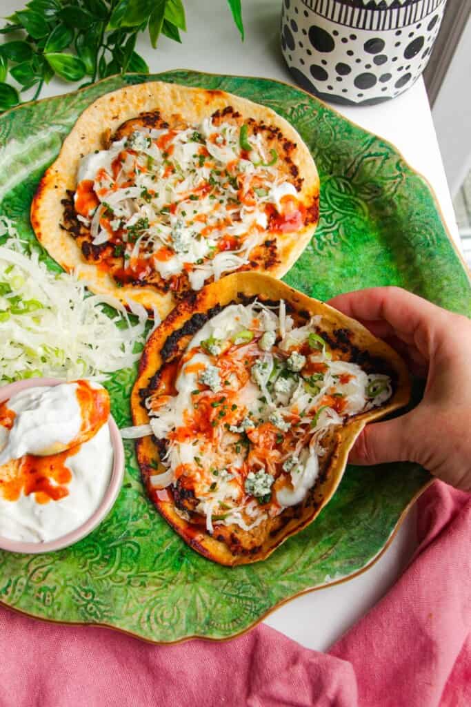 Hand picking up buffalo chicken smash taco from platter.