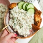 Hand holding plate with Caesar inspired chicken salad, with pita chips and cucumber on the side.