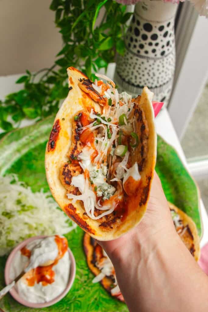Holding a buffalo chicken taco with more in the background.