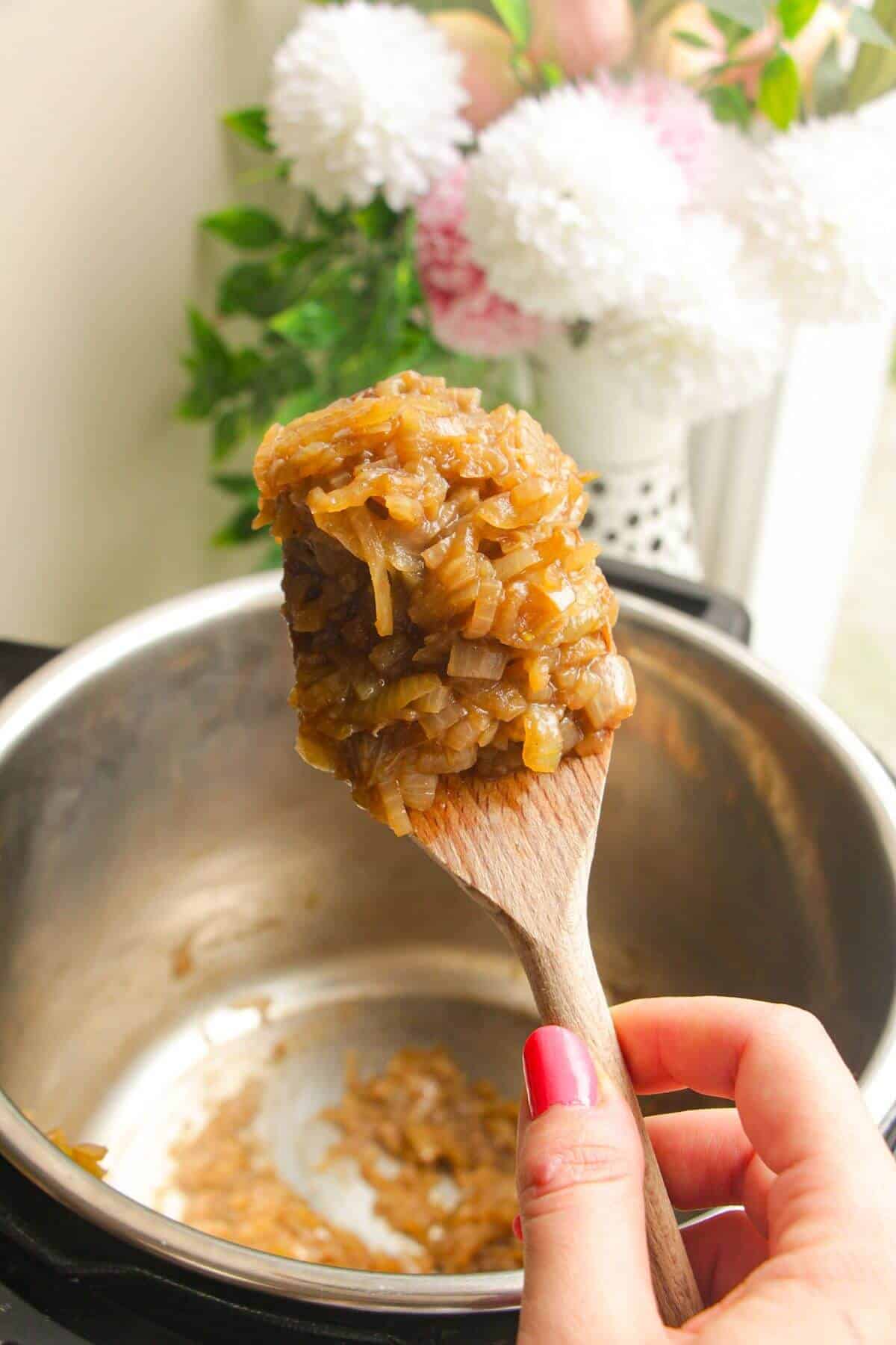Wooden spoon with caramelized onions, with Instant Pot in the background.
