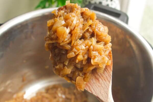 Wooden spoon with caramelized onions, with Instant Pot in the background.