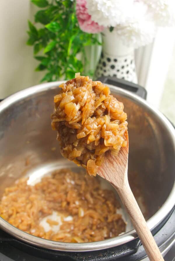 Wooden spoon with caramelized onions, with Instant Pot in the background.