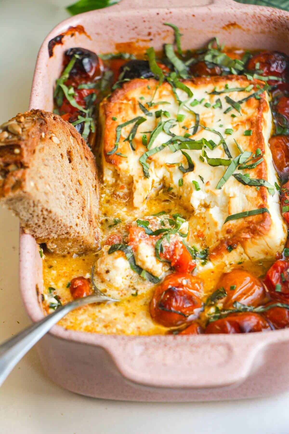 Jammy baked feta and tomato dip in an oven dish, with a slice of bread.