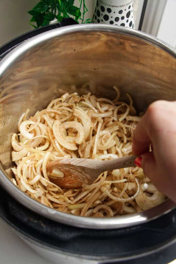 Stirring sliced onions with a wooden spoon in Instant Pot.