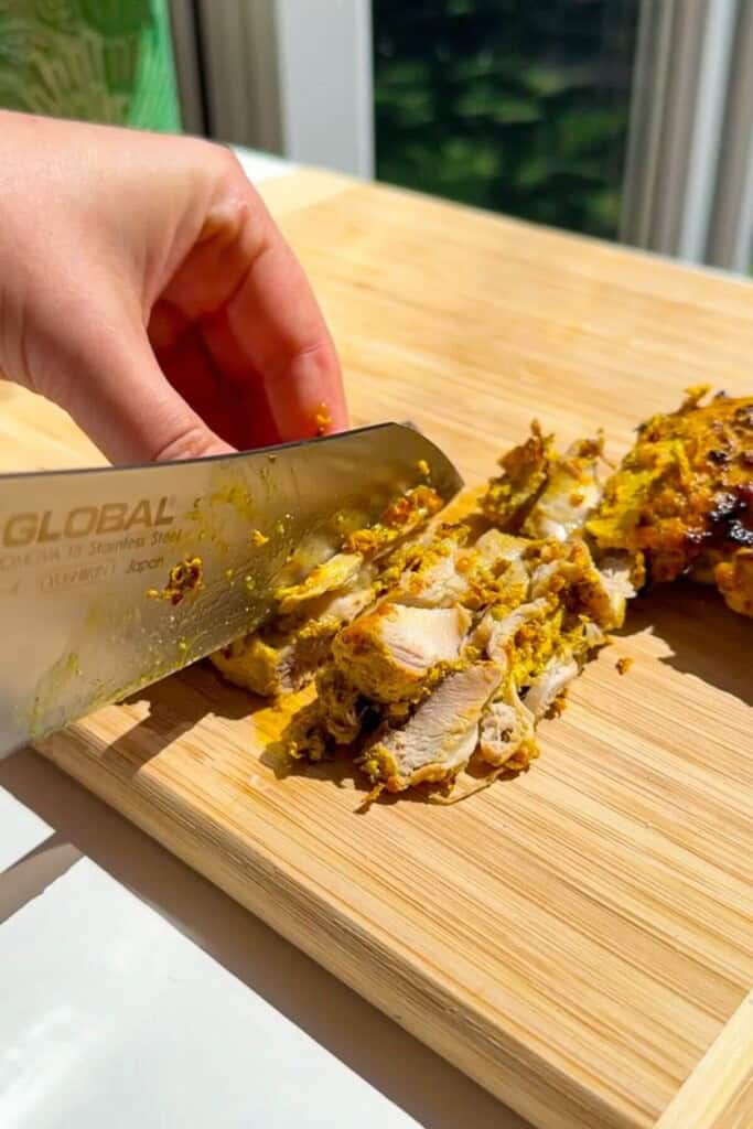 Chopping Greek chicken thighs thinly.