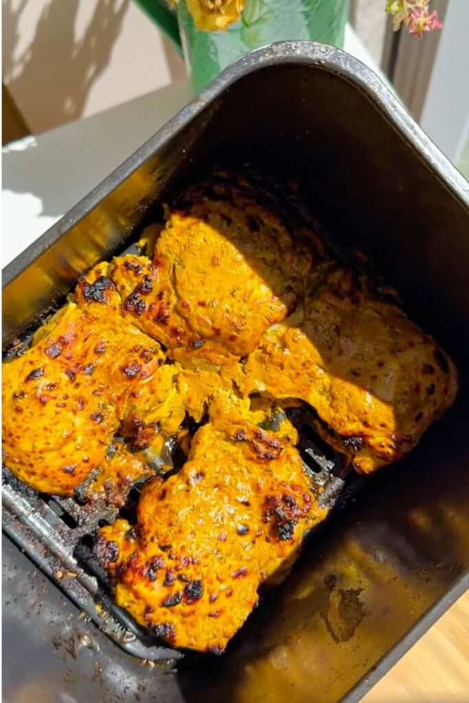 Cooked Greek chicken thighs in air fryer basket.