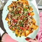 Hand holding platter of Greek pita nachos.