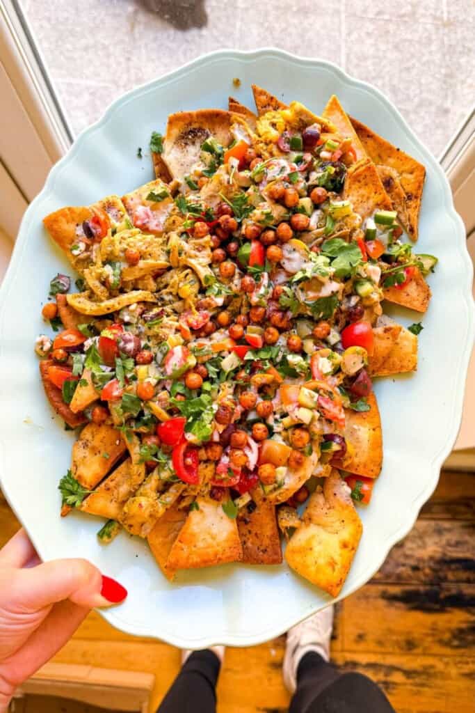 Hand holding platter of Greek pita nachos.