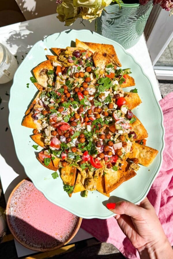 Hand holding platter of Greek pita nachos.