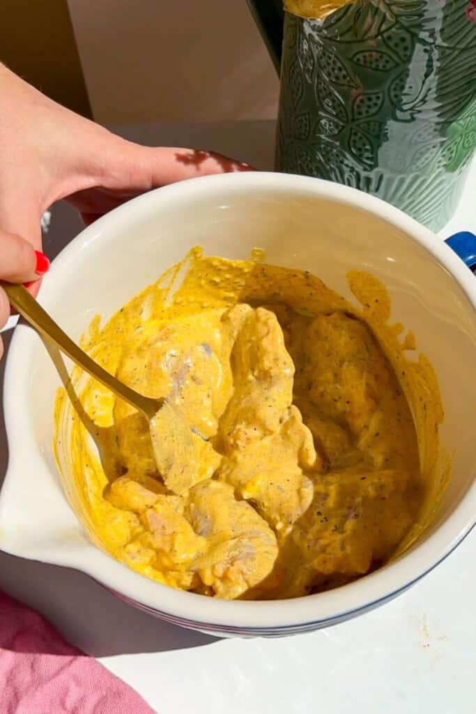 Chicken thighs tossed with Greek marinade in a bowl.