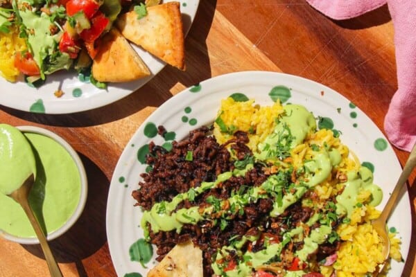 Two Mediterranean beef rice bowls, with green tahini sauce on the side.